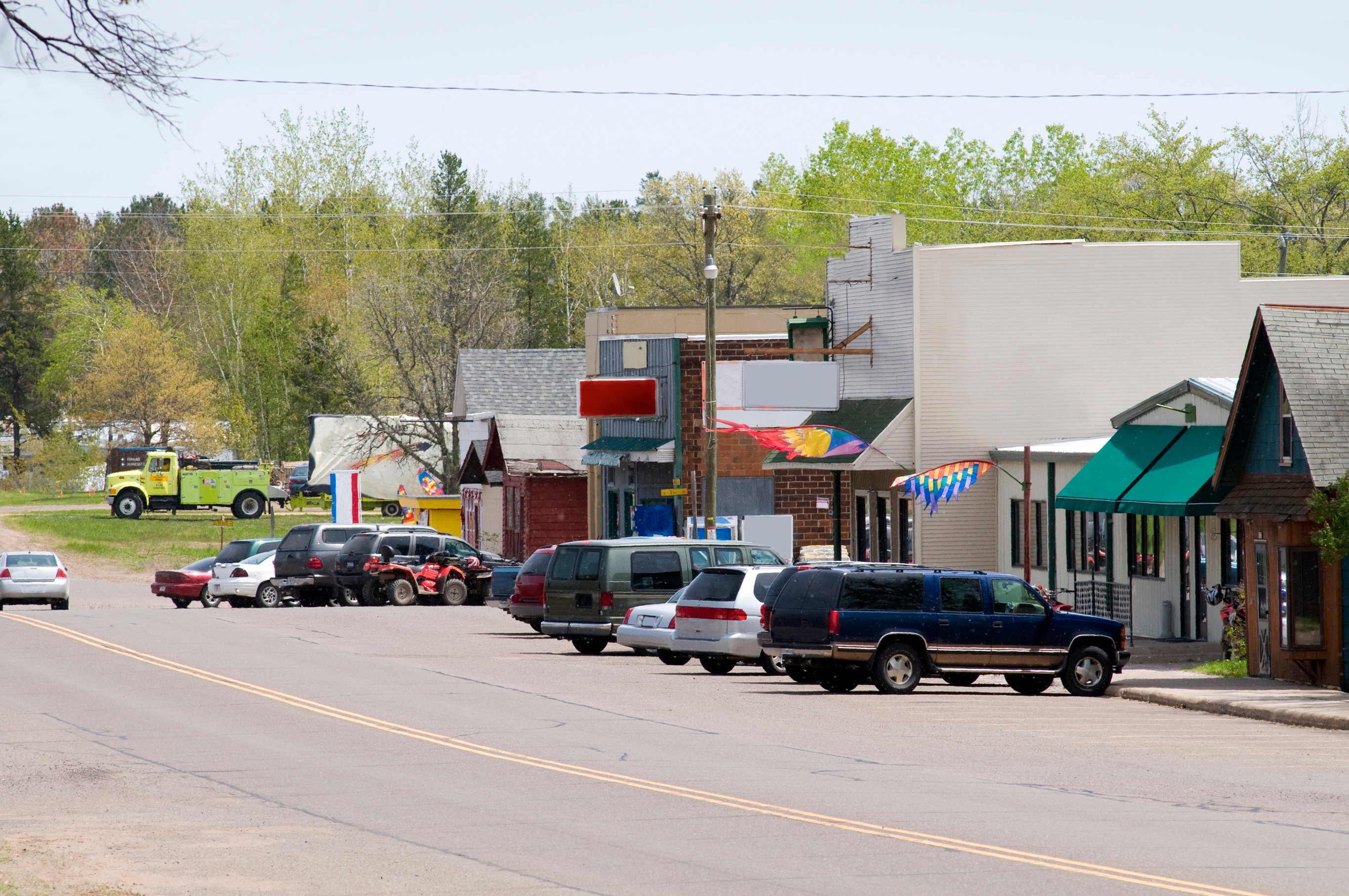 Small town street scene with parked cars, a fire truck in the distance, and buildings with storefronts and colorful signs