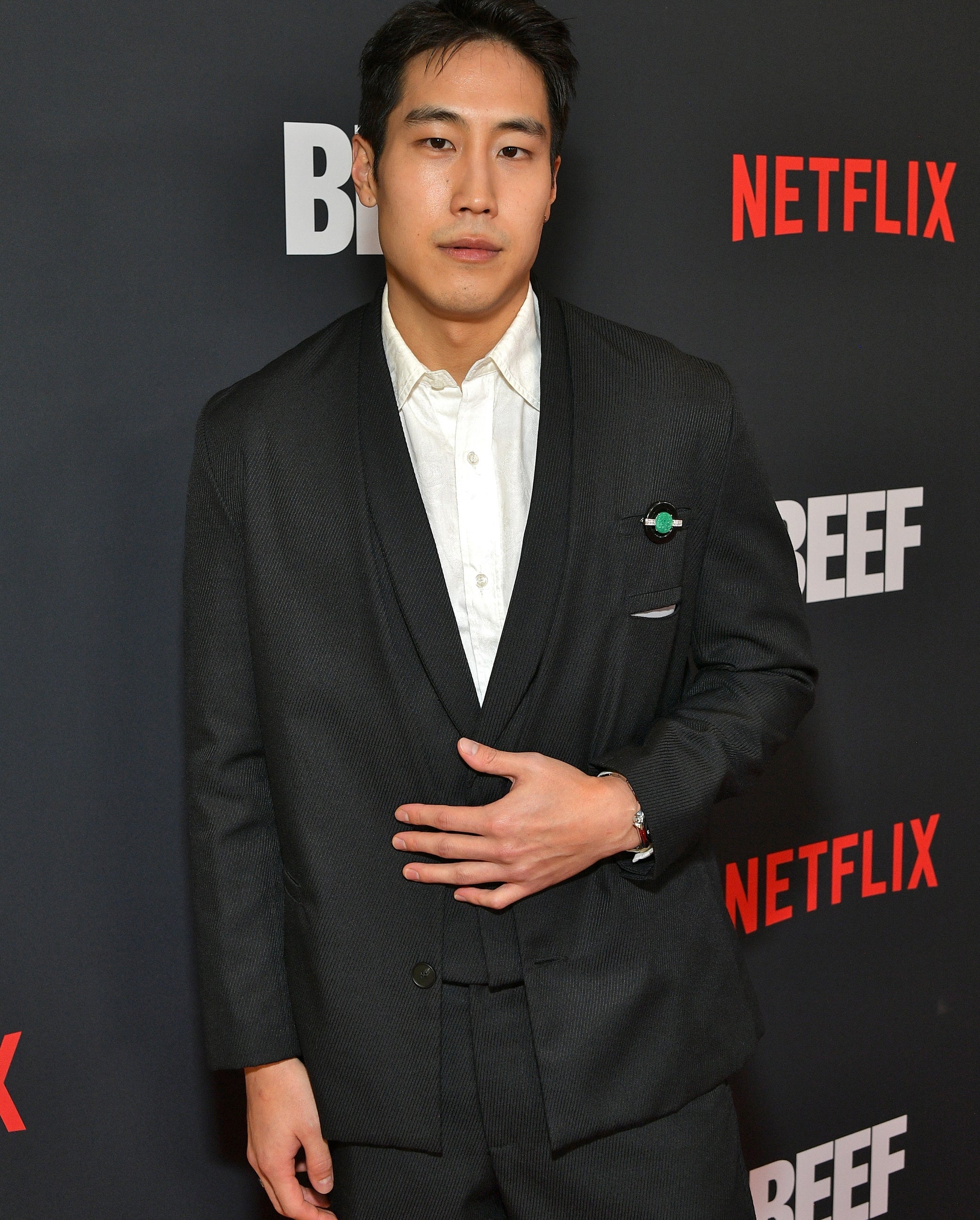 Young Mazino in a formal suit poses at a Netflix event for "Beef," standing in front of a branded backdrop