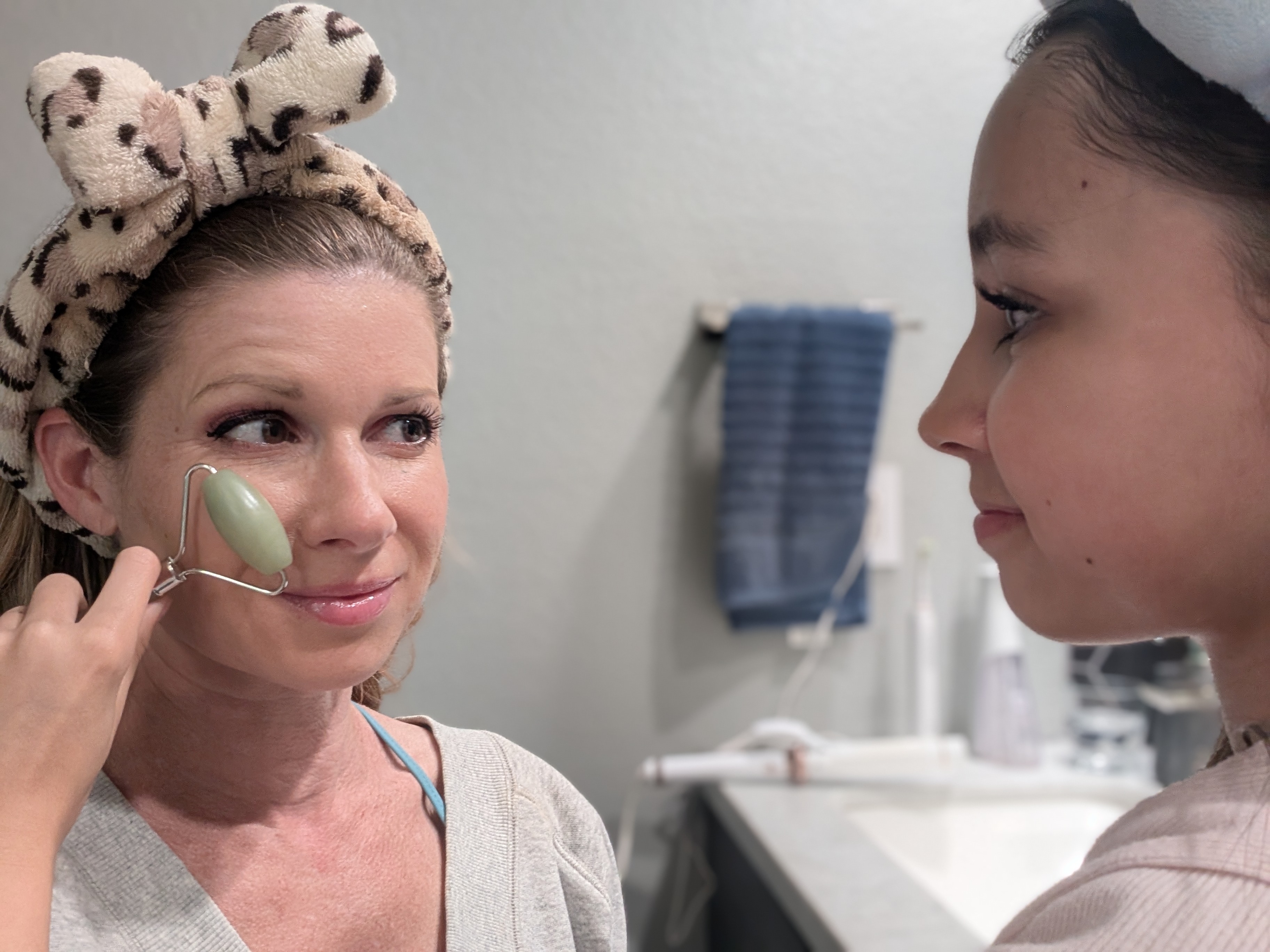 Young girl uses jade roller to give her daughter a facial in the bathroom