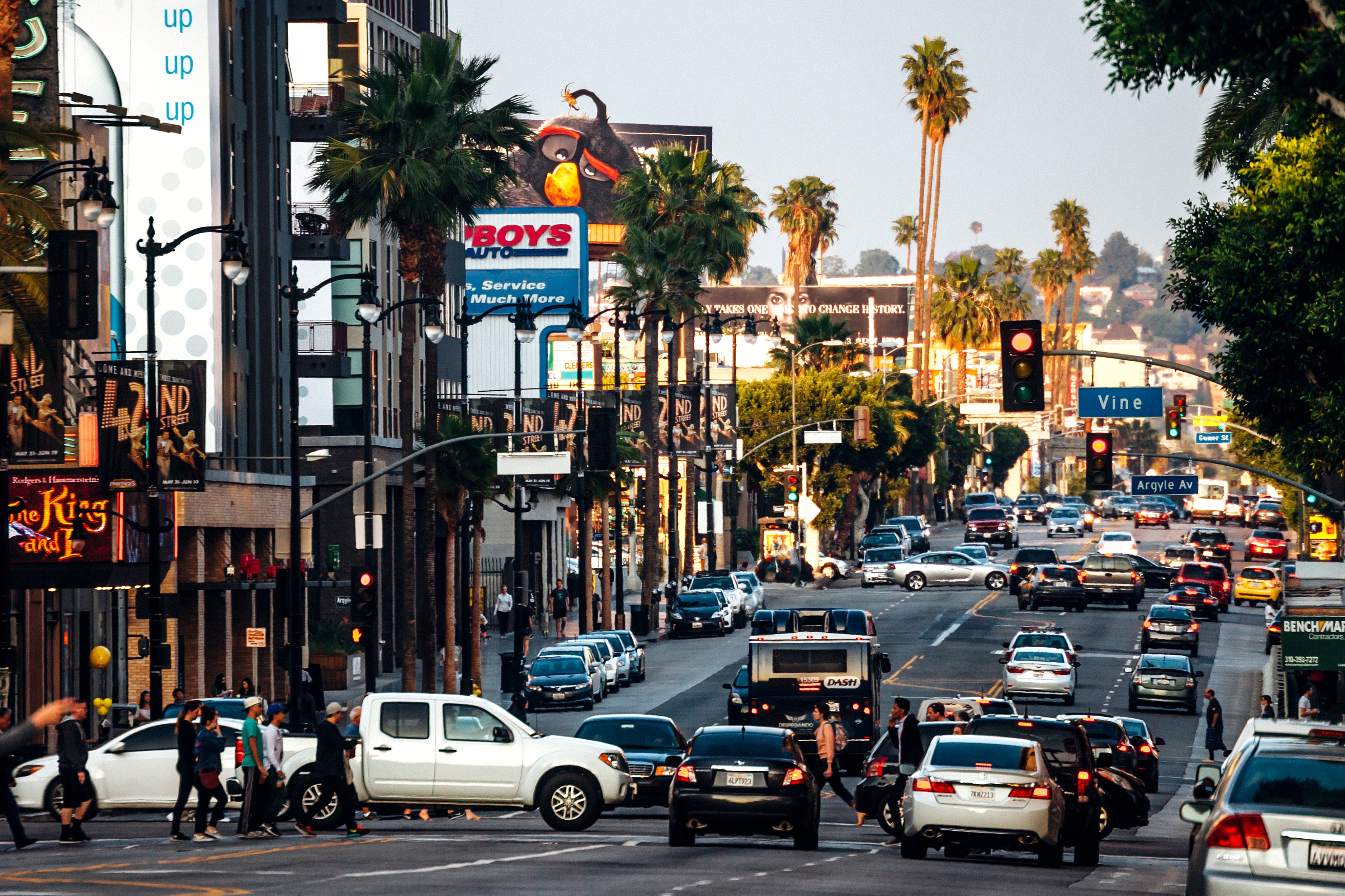 Bustling Los Angeles street scene with heavy traffic, pedestrians, palm trees, and various storefronts lining the road
