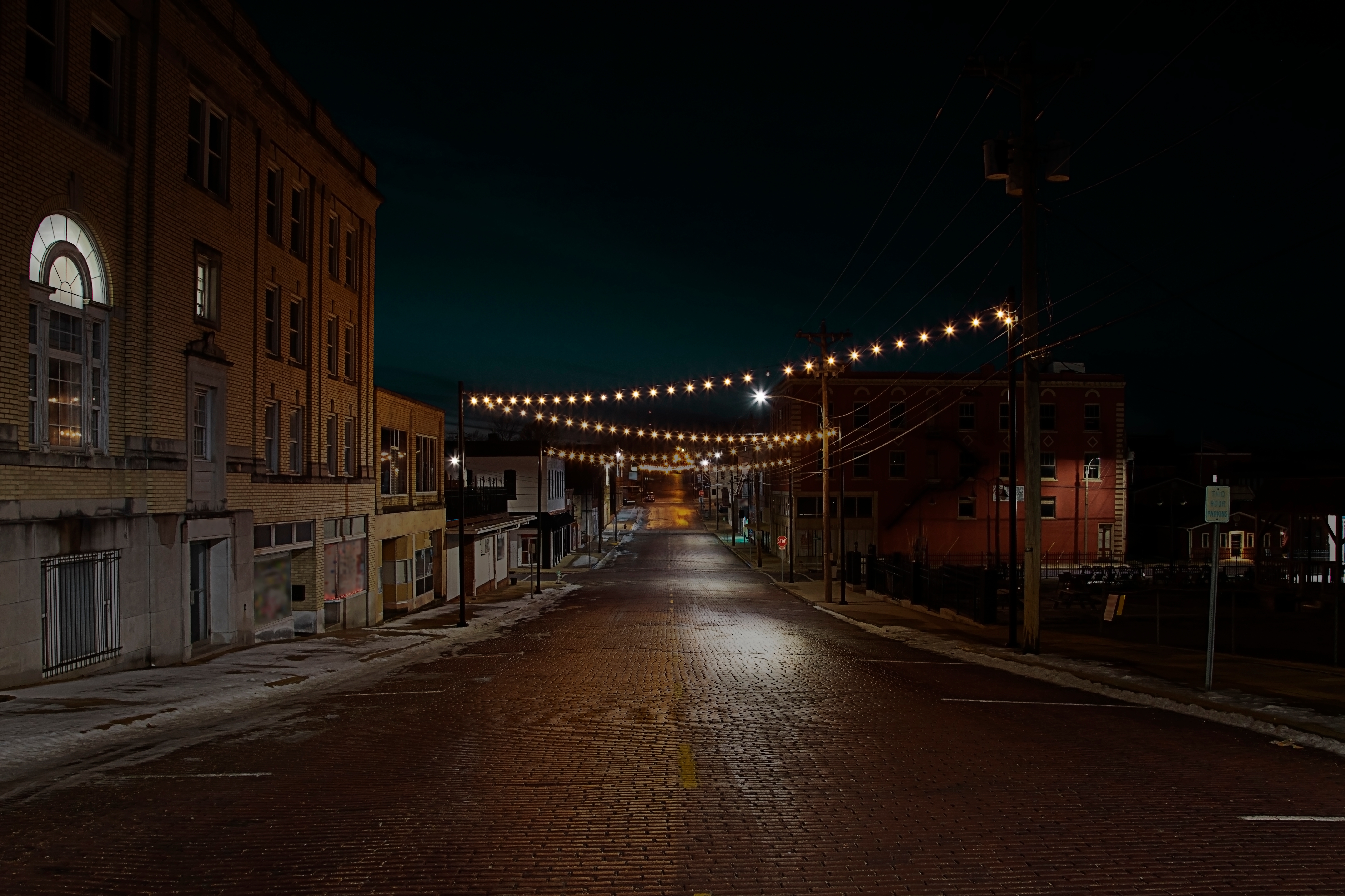 A quiet, empty street at night with buildings on both sides, illuminated by overhead string lights