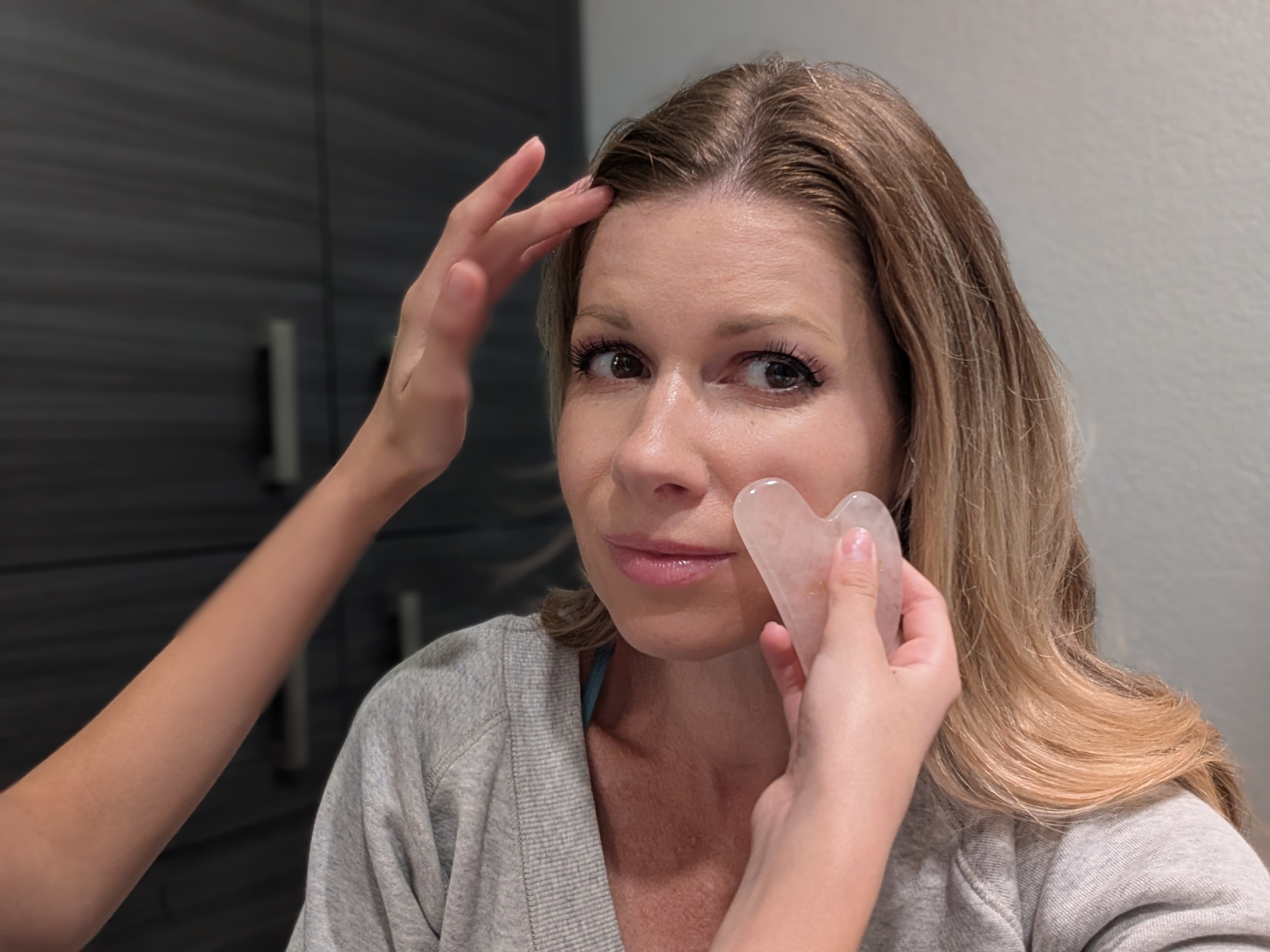 A woman sitting while receiving a skincare treatment with a facial tool under her eye and someone gently touching her forehead