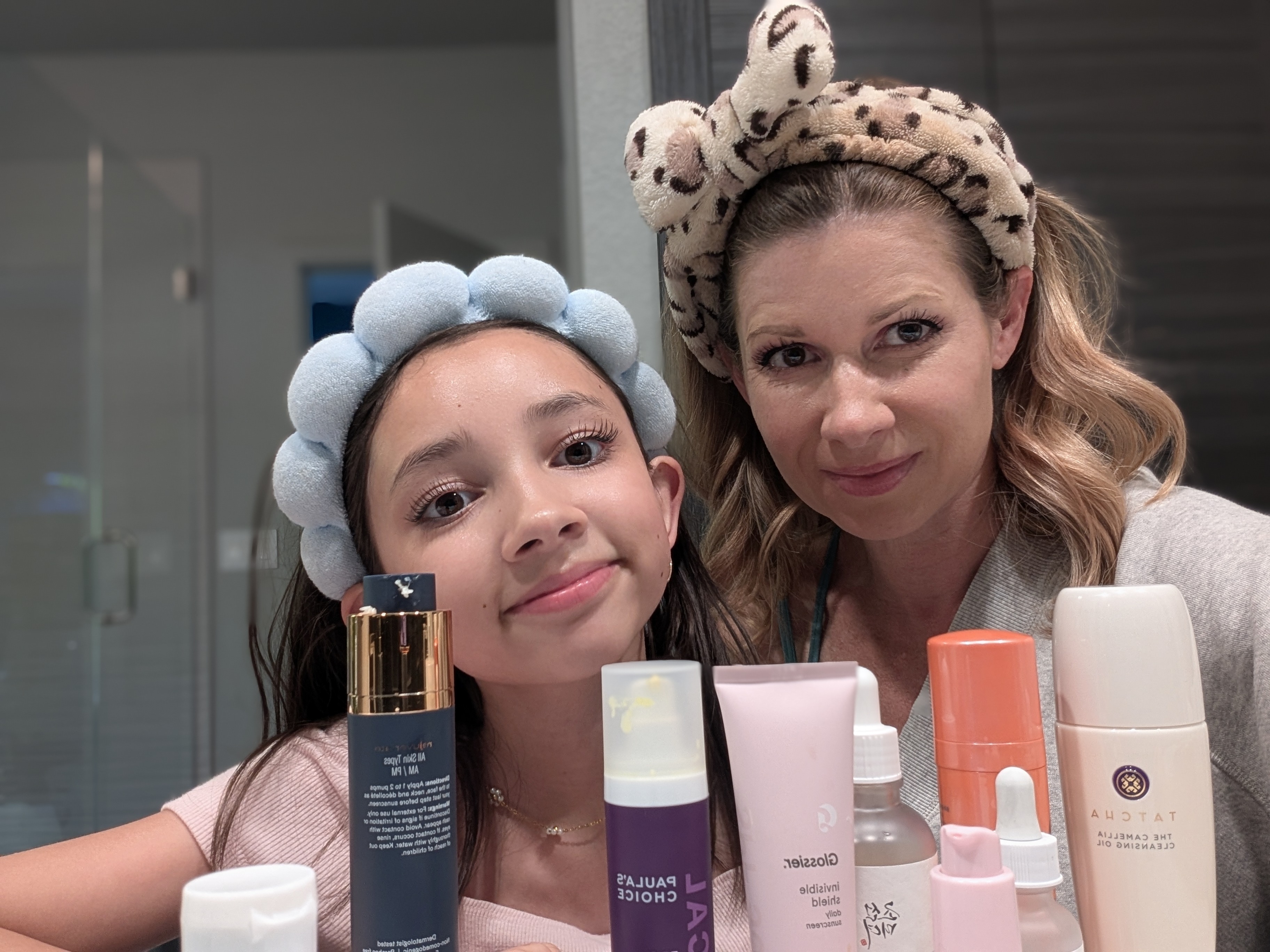 Mother and daughter look into the mirror with a collection of skincare products in front of them