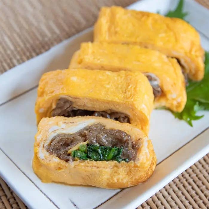 肉と野菜の具が詰まった卵焼きが白い皿に並んでいる。