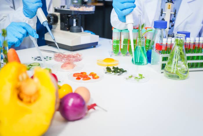 Scientists working with food samples and lab equipment, including pipettes, test tubes, and various produce, in a laboratory setting