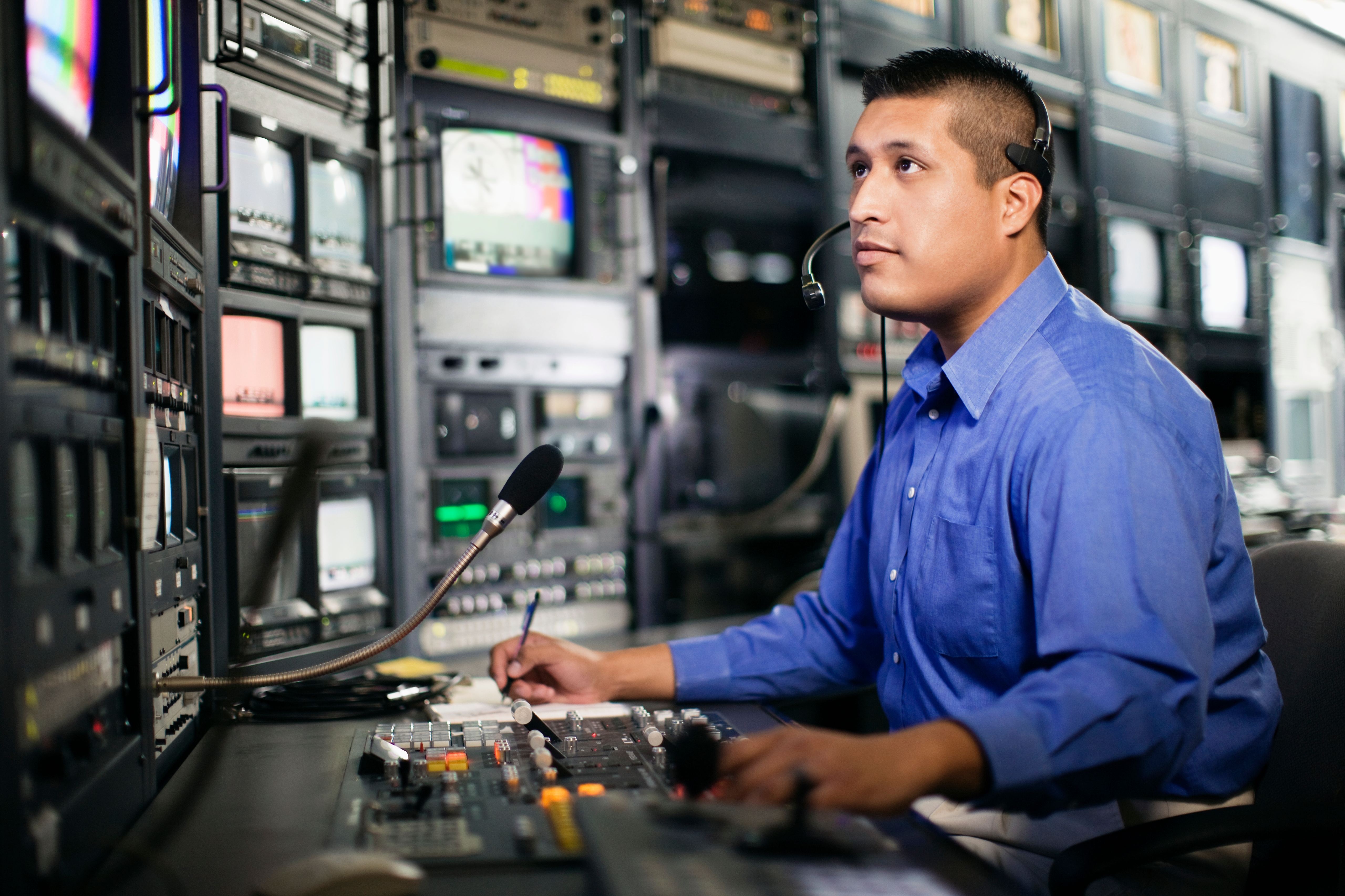 Person in a broadcast control room wearing a headset, operating audio and video equipment