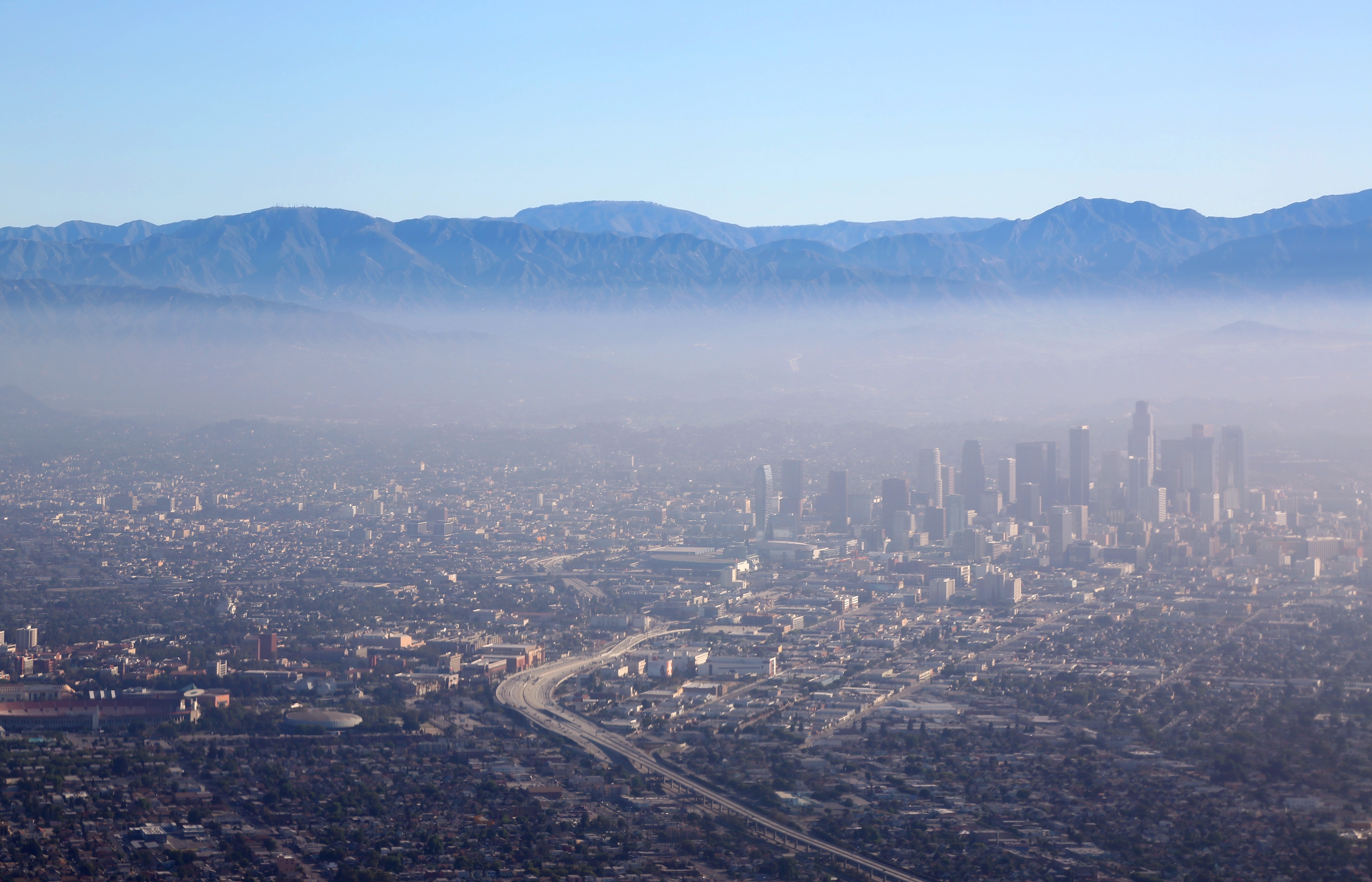 Aerial view of a cityscape with tall buildings and highways, surrounded by mist and mountains in the background