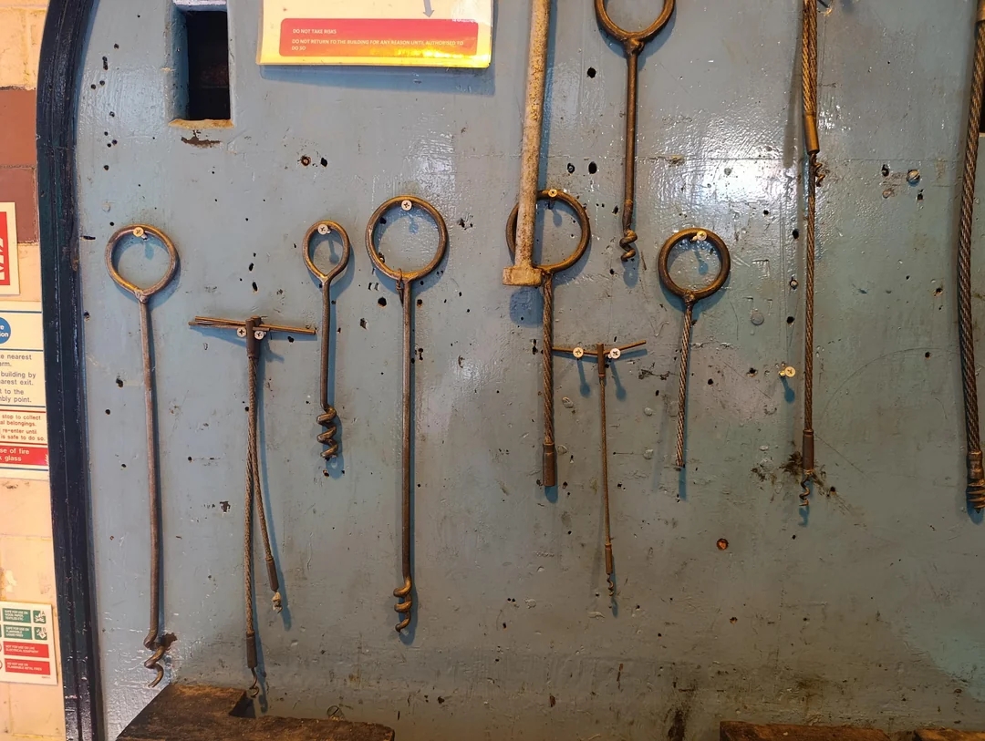Assorted vintage metal tools hang on a blue wall, showcasing various designs and sizes