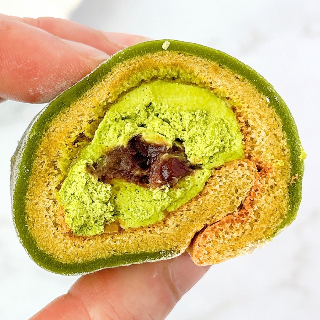 指で持たれた抹茶とあんこ入りのロールケーキの断面。