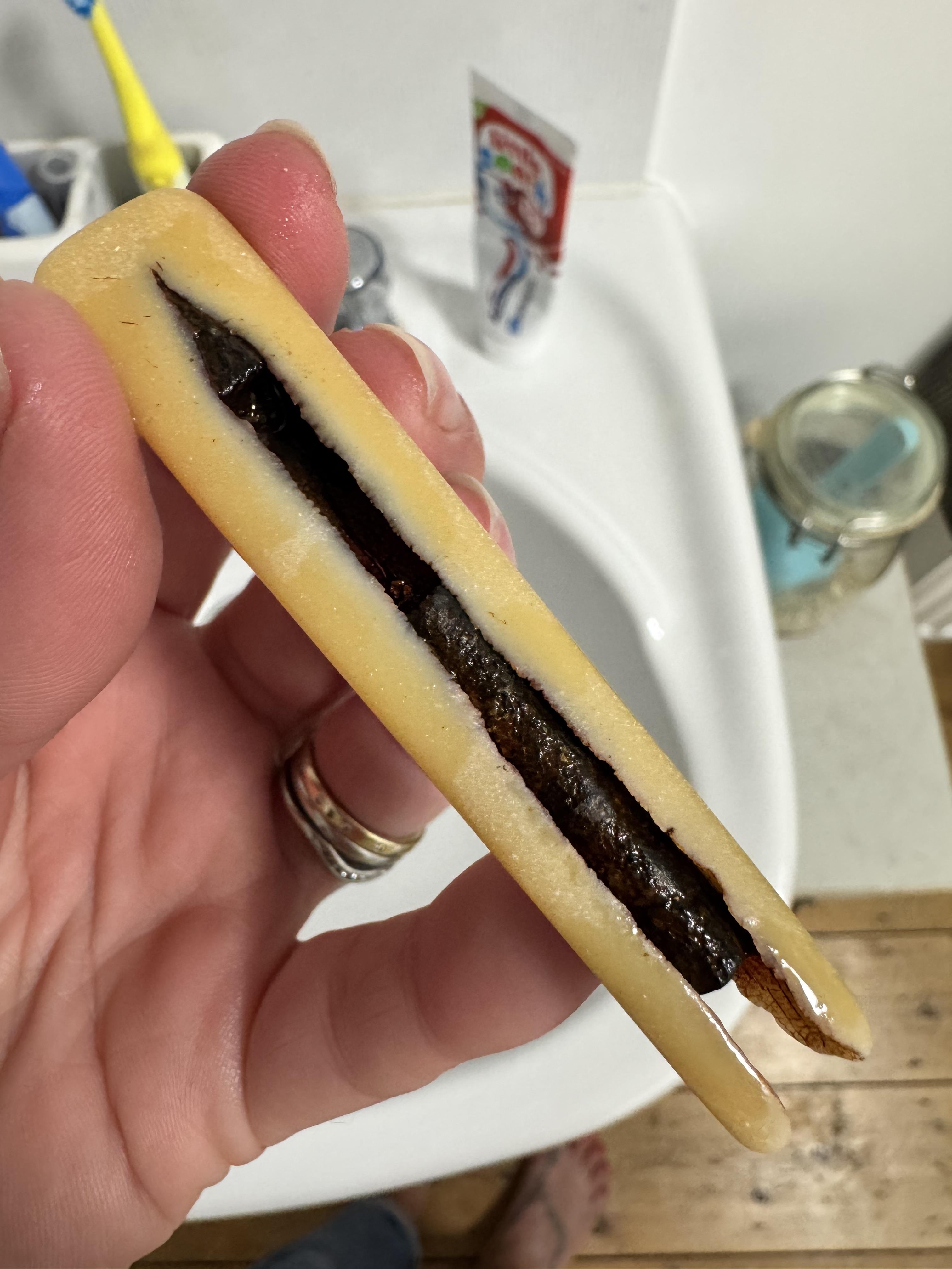 Hand holding a tube-shaped item with two sides surrounding a central piece. Background is a sink and hygiene items