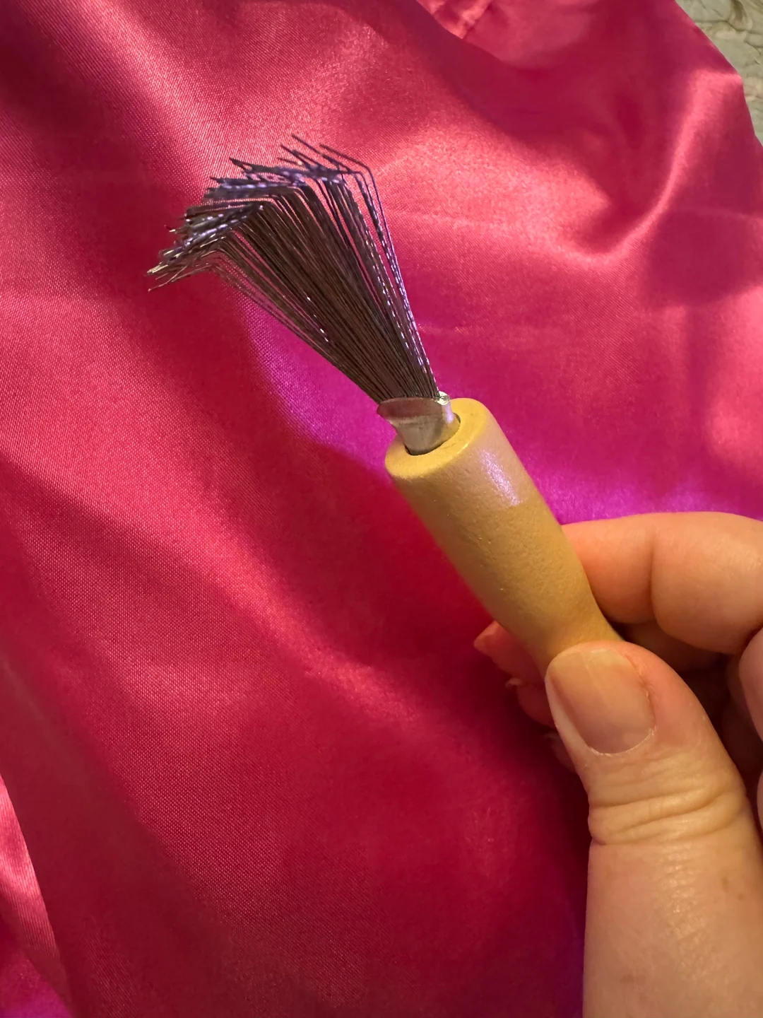 A hand holding a felting needle tool with multiple sharp prongs, set against a pink fabric background