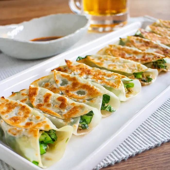 お皿に整然と並んだ焼き餃子があり、奥には醤油のソース皿とビールのグラスが置かれています。