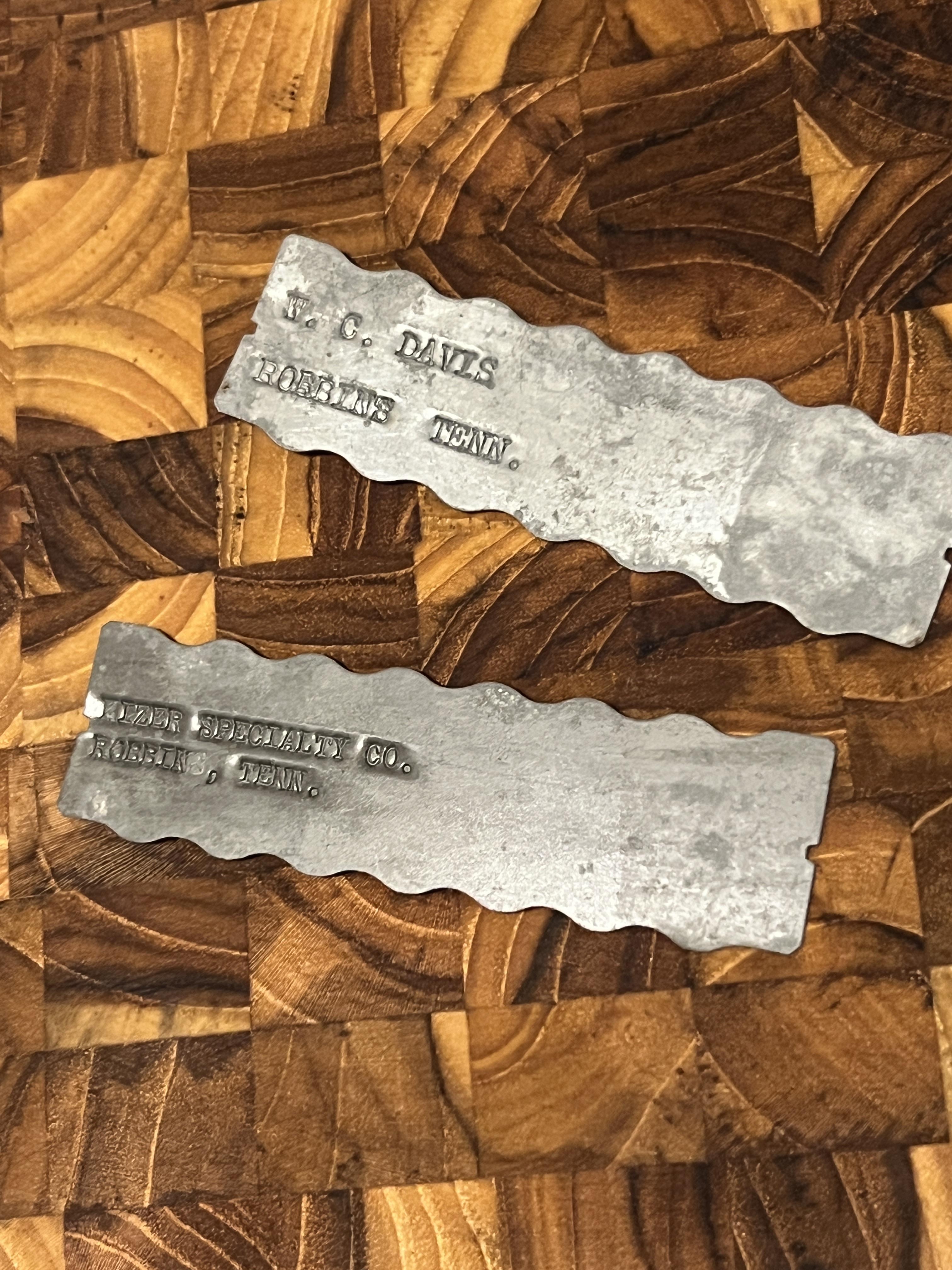 Two metal ID plates with stamped text on a wooden surface; details are unclear from the image