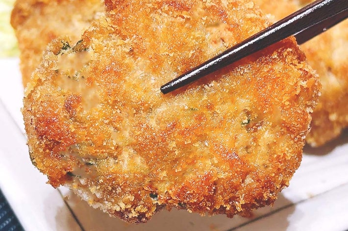 箸で持たれたサクサクのフライ、食欲をそそる一品が皿に盛られている。