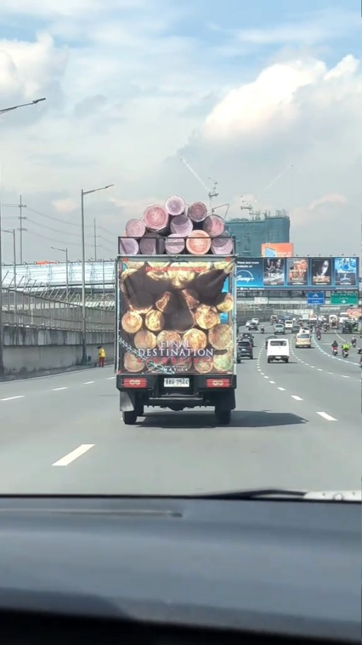 Truck on highway carries logs; back advert shows logs perfectly aligned into pizza slices, creating illusion of stacked pizzas on top of truck