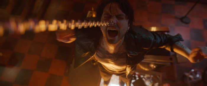 A person in a dramatic scene appears to be yelling, standing under a suspended chain above