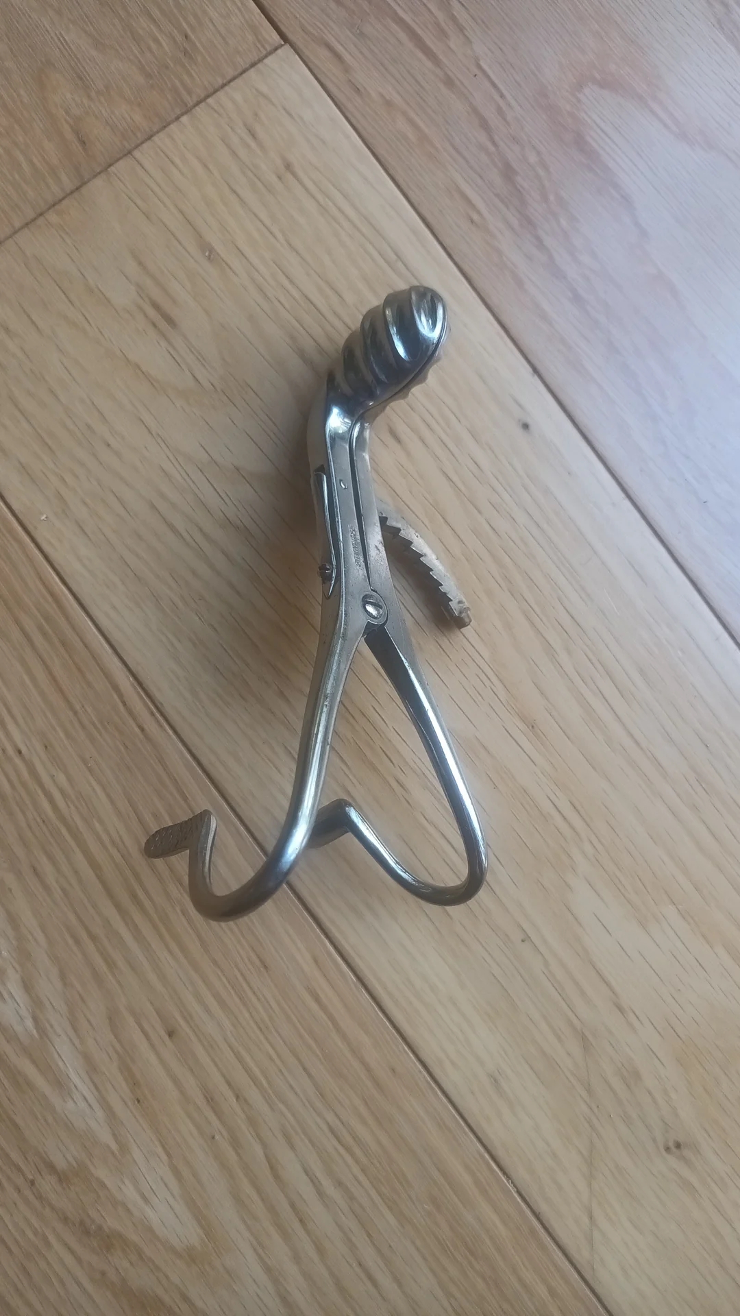 Hand-crank apple peeler on a wooden floor, showing its metal gear and blade