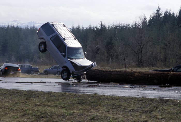 SUV crashing into a fallen tree on a highway, impacting front-first and lifted off the ground; other vehicles are visible in the background