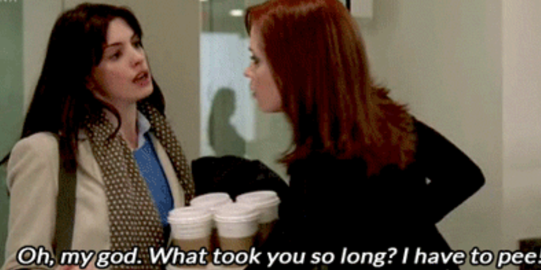 Two women talking, one holding several coffee cups. Text: "Oh, my God. What took you so long? I have to pee!"