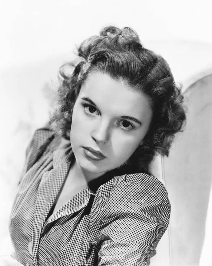 A person with 1940s-style curled hair poses in a polka-dot blouse, gazing directly at the camera