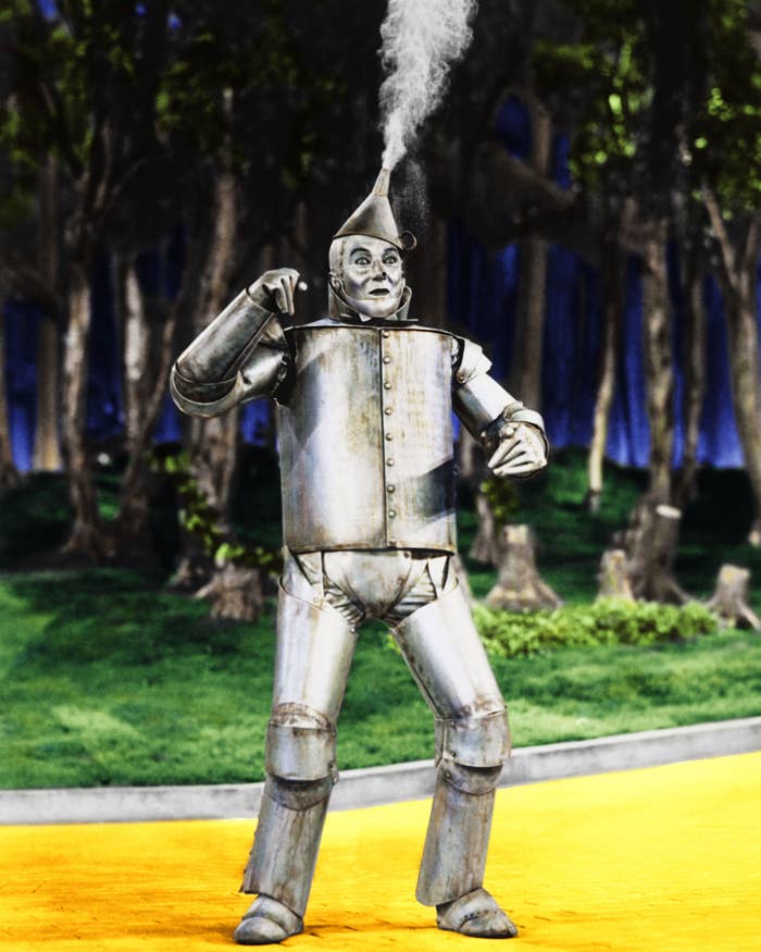 Tin Man, from "The Wizard of Oz," stands on the yellow brick road in a forest setting, with steam coming from his hat