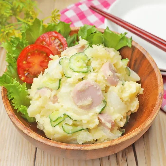 木製ボウルに盛られたポテトサラダ。トマトとレタスが添えられ、上にスライスしたきゅうりが乗っている。