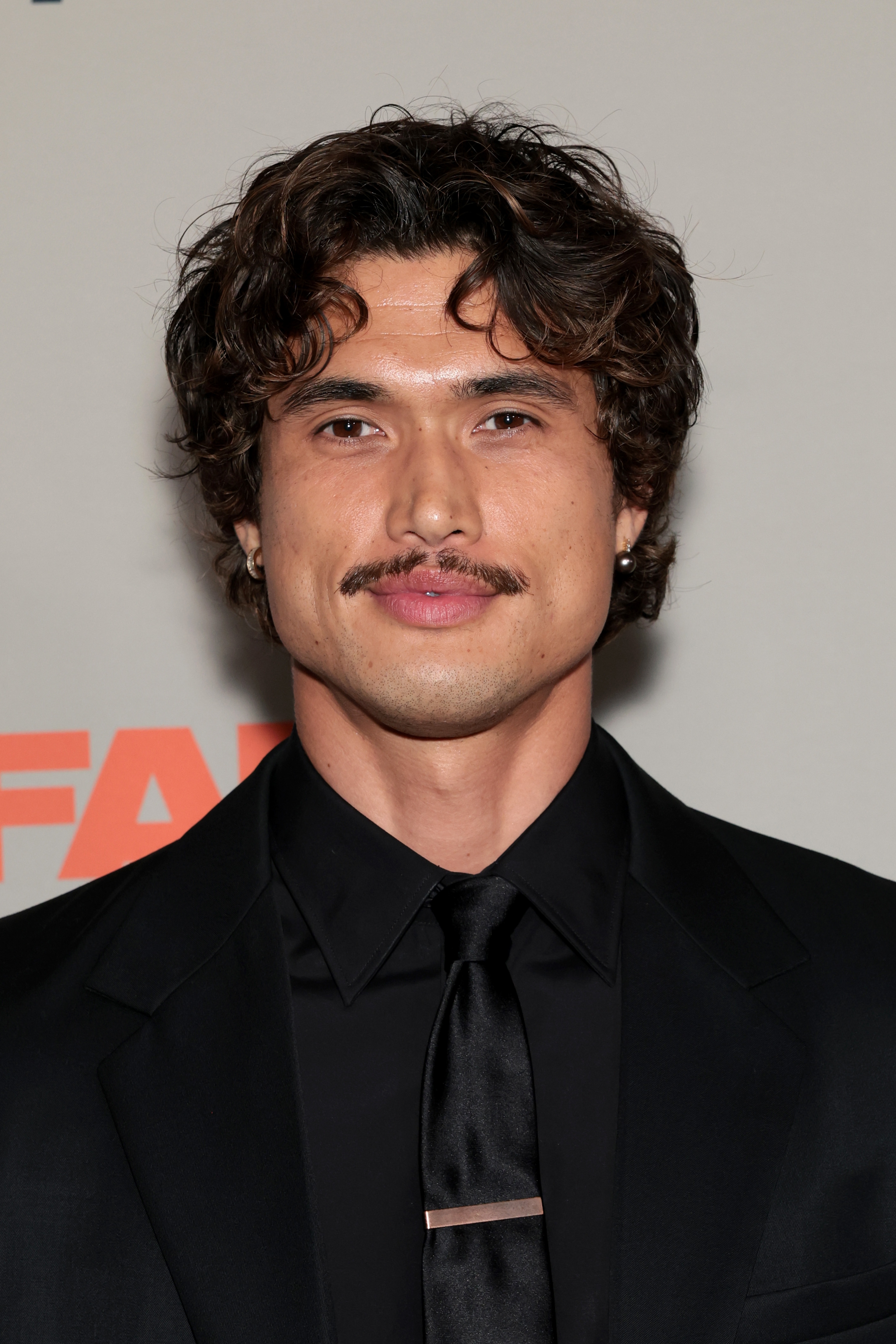 Person in formal suit with wavy hair and a mustache at an event