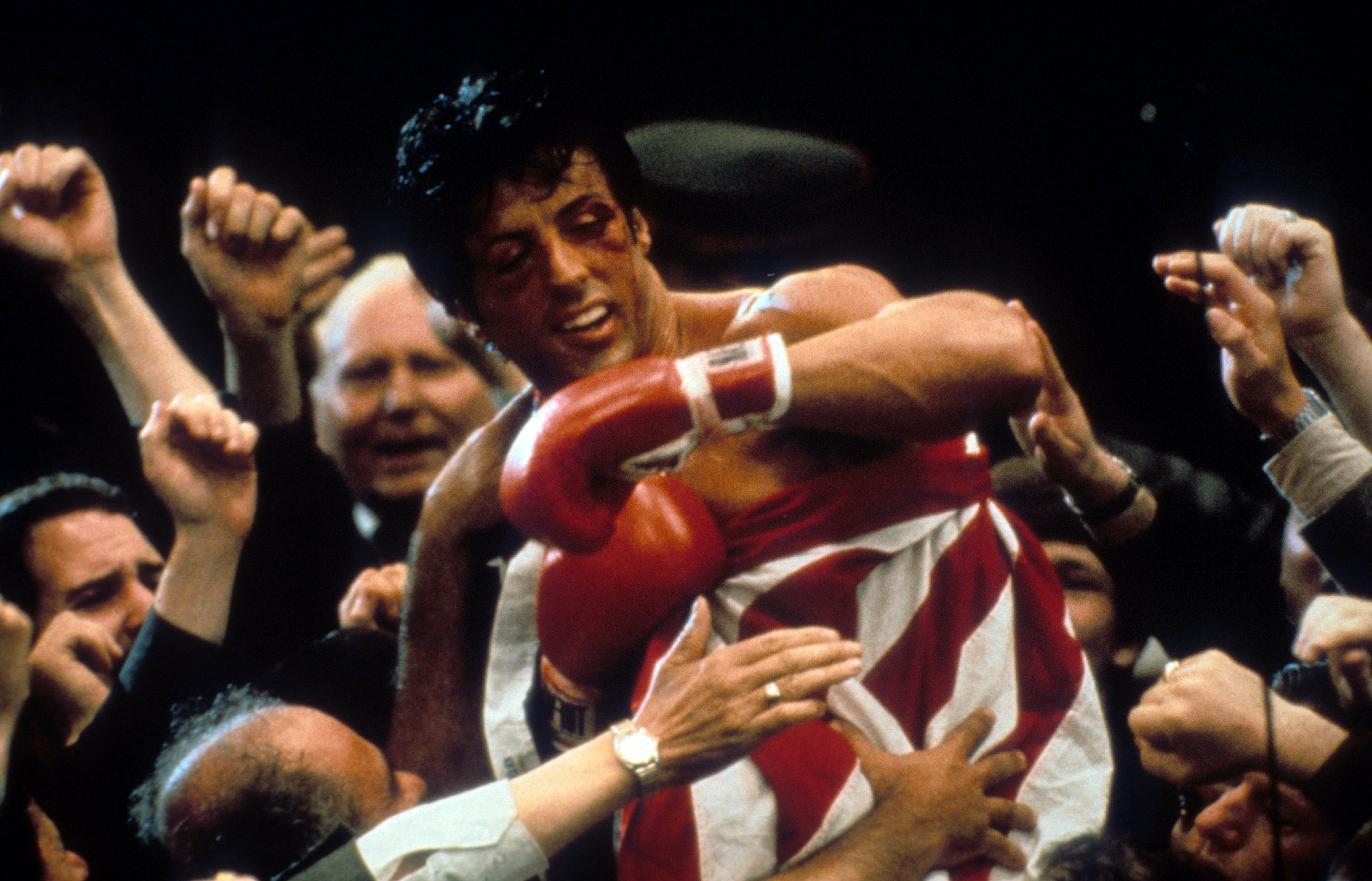 Boxer in the ring, surrounded by cheering crowd, wearing a robe with stripes, celebrating a victory