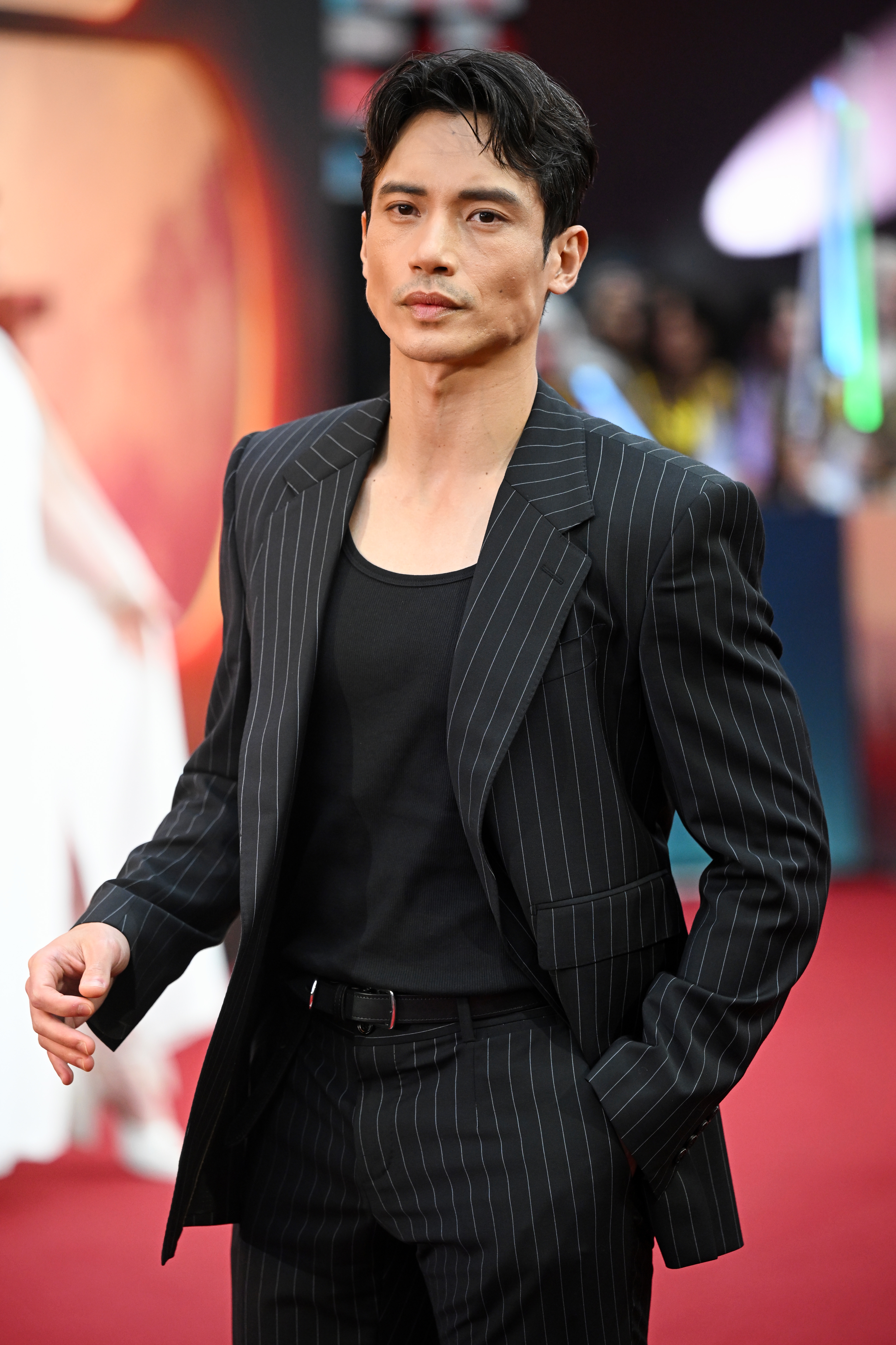 A person in a pinstripe suit and black shirt poses on a red carpet