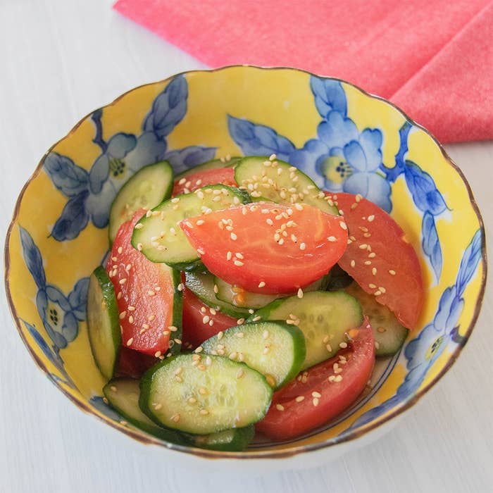 きゅうりとトマトのサラダが花柄の器に入っている。上にはゴマがかけられている。