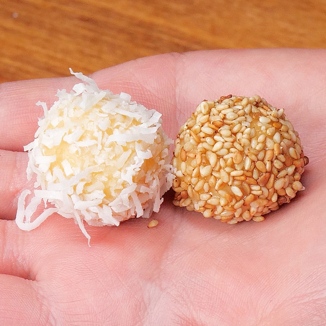 手のひらにココナッツフレークとごまをまぶした2つの異なるトリュフが乗っている。