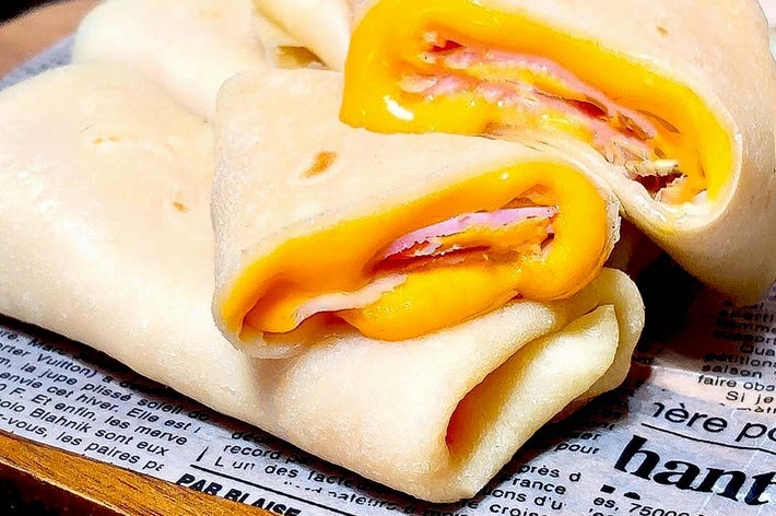 木のトレイにハムとチーズ入りクレープが並んでいます。クレープは新聞風の紙の上に置かれています。