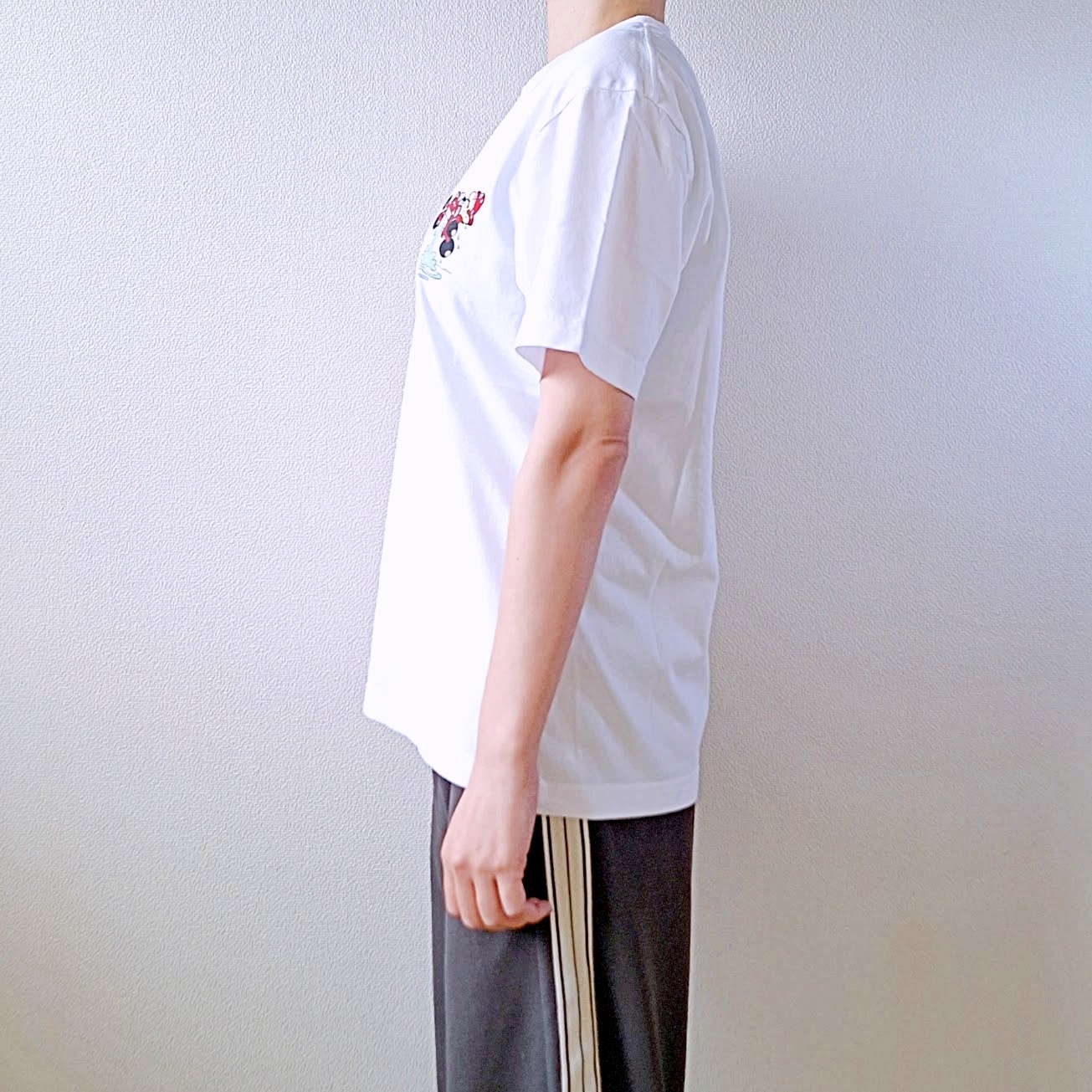 人物がTシャツとストライプのパンツを着て横を向いて立っている側面の写真。