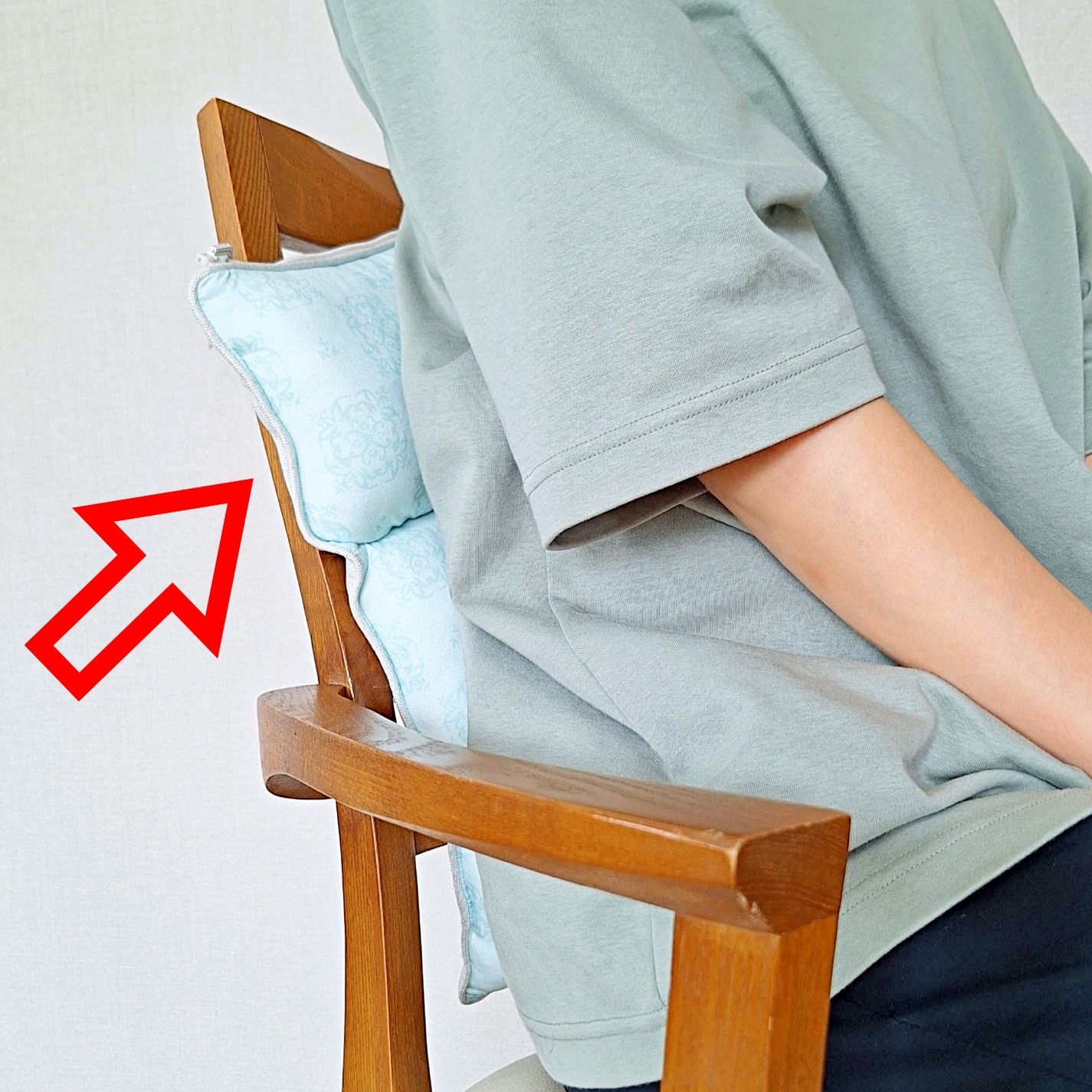 椅子に寄りかかり、クッションを使って快適な姿勢を取っている人の横からの様子。赤い矢印がクッションを指している。