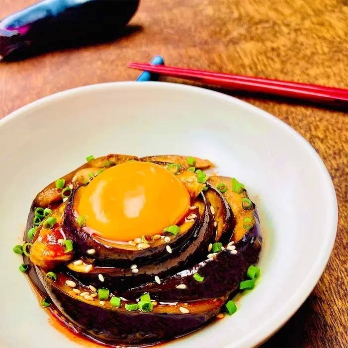 卵黄とナスのスライスが白い皿に盛り付けられ、ネギとゴマがトッピングされています。