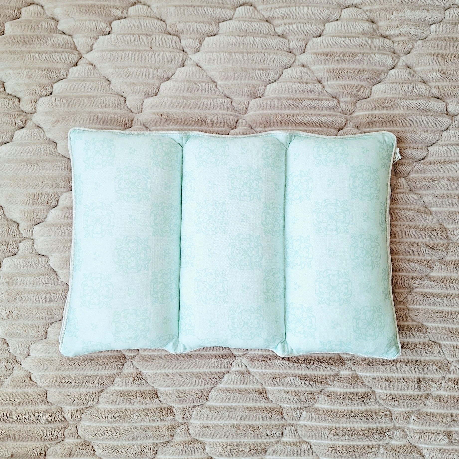 ベージュのキルティングカーペット上に置かれた、柔らかそうな白い枕。