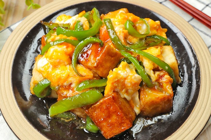 中華風の野菜と豆腐の炒め物が黒い皿に盛り付けられ、テーブルに置かれている。