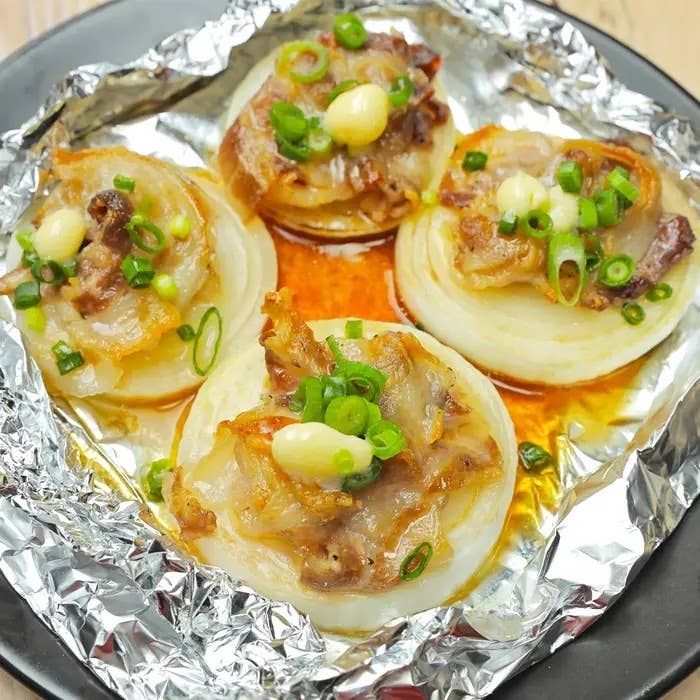 ホイルにのった玉ねぎの焼き料理。ベーコン、バター、ネギがトッピングされている。