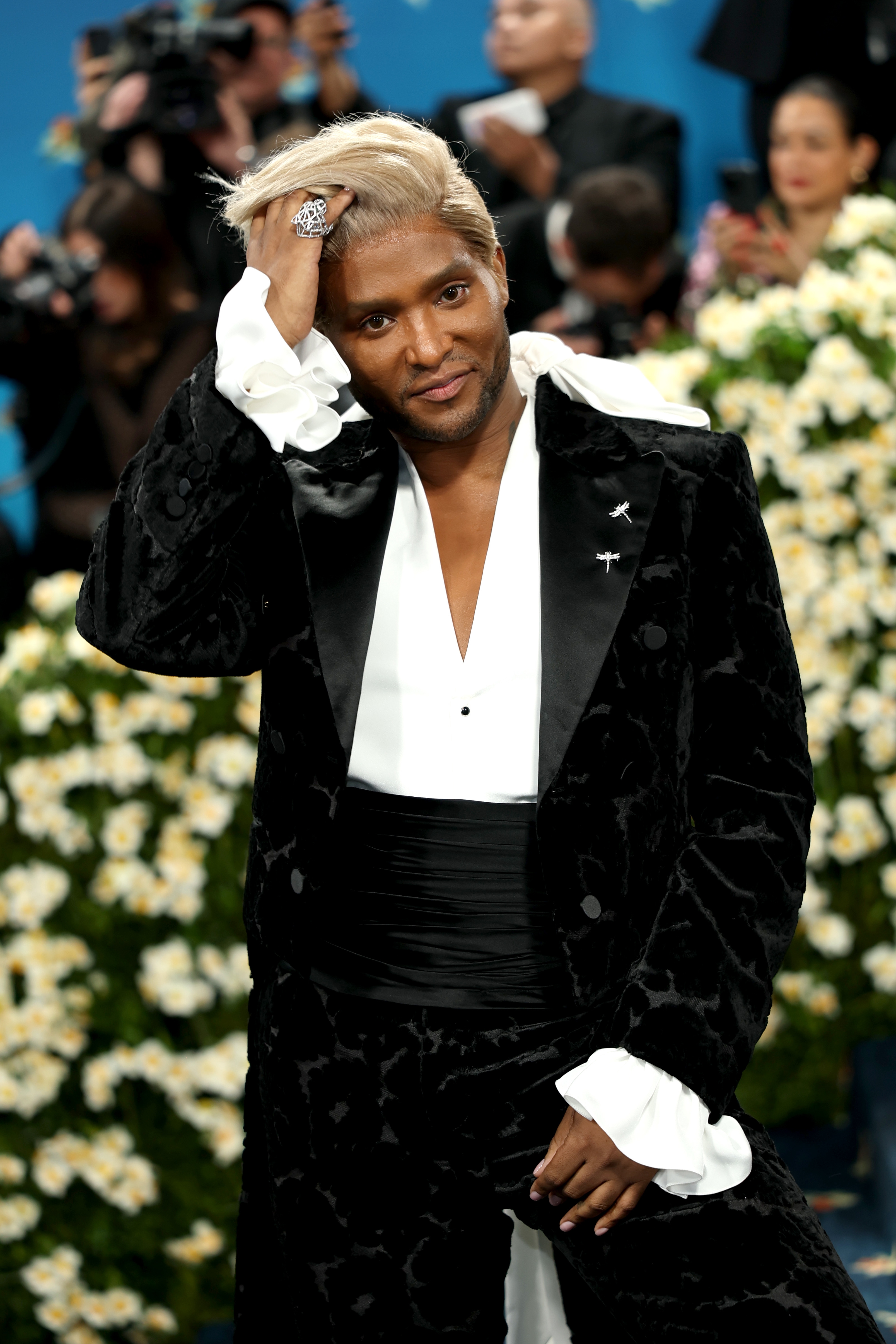 Law Roach on the Met Gala red carpet wearing a velvet suit with a ruffled shirt, running hand his hair