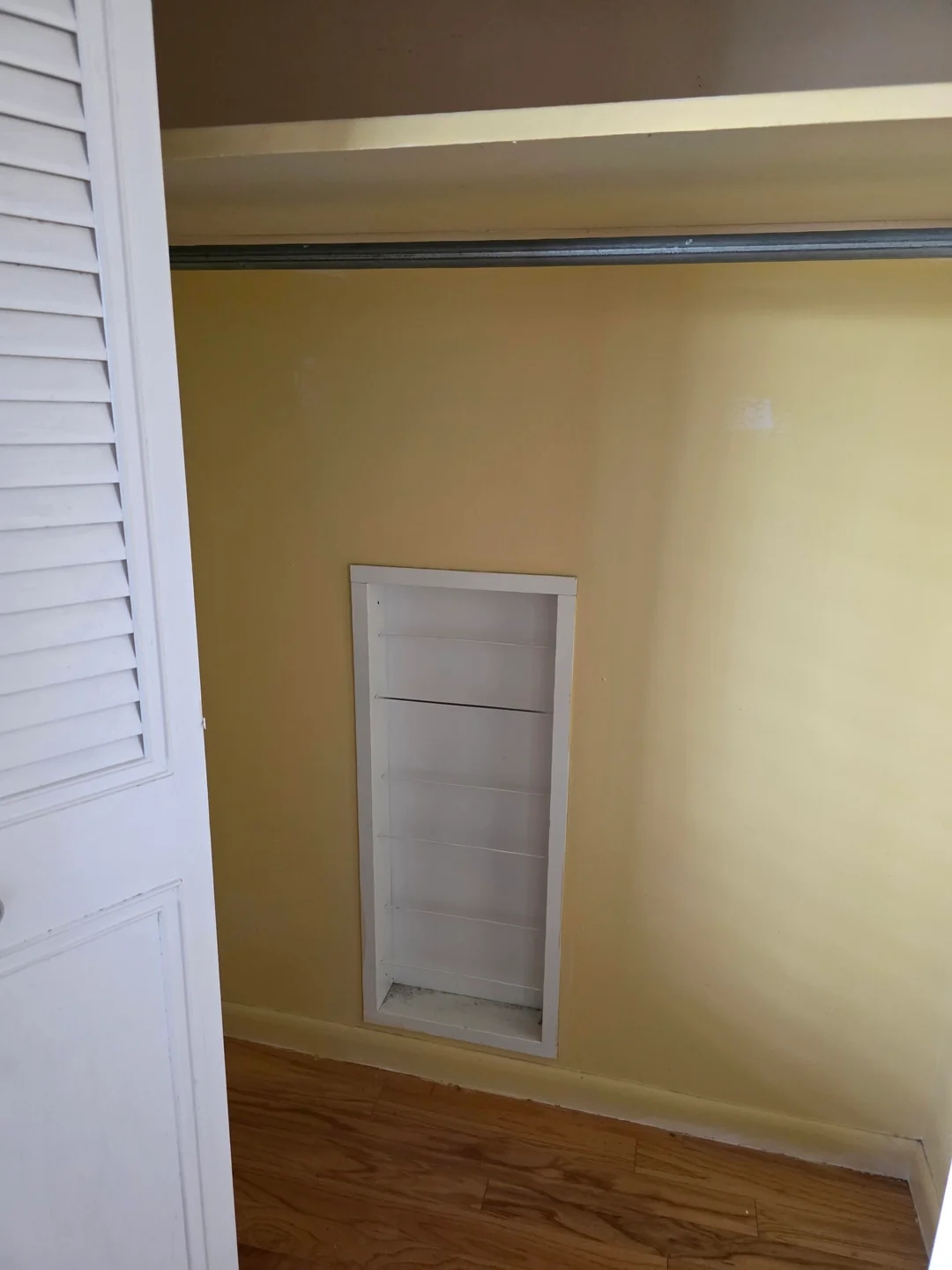 Small nook in an empty closet with wooden flooring and a yellow wall