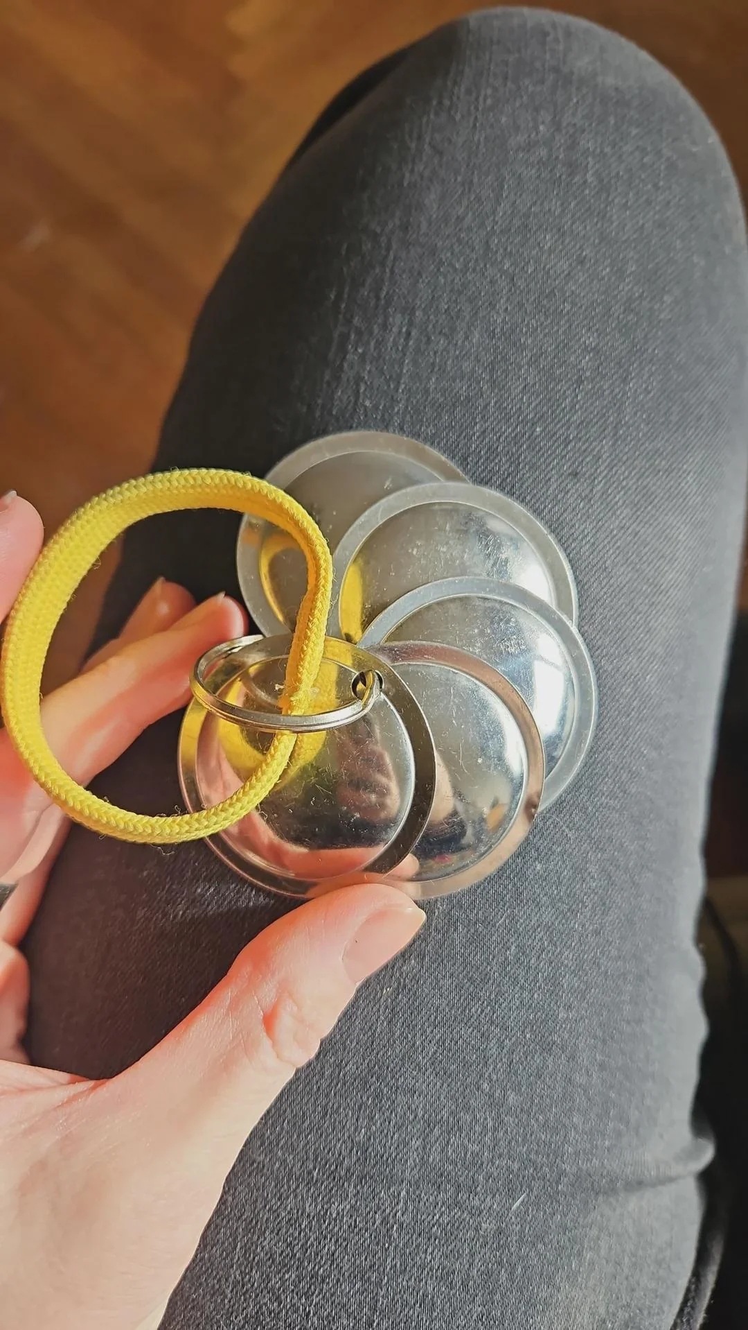 Person holding a cluster of shiny, round metallic objects tied together with a yellow string, resting on their leg