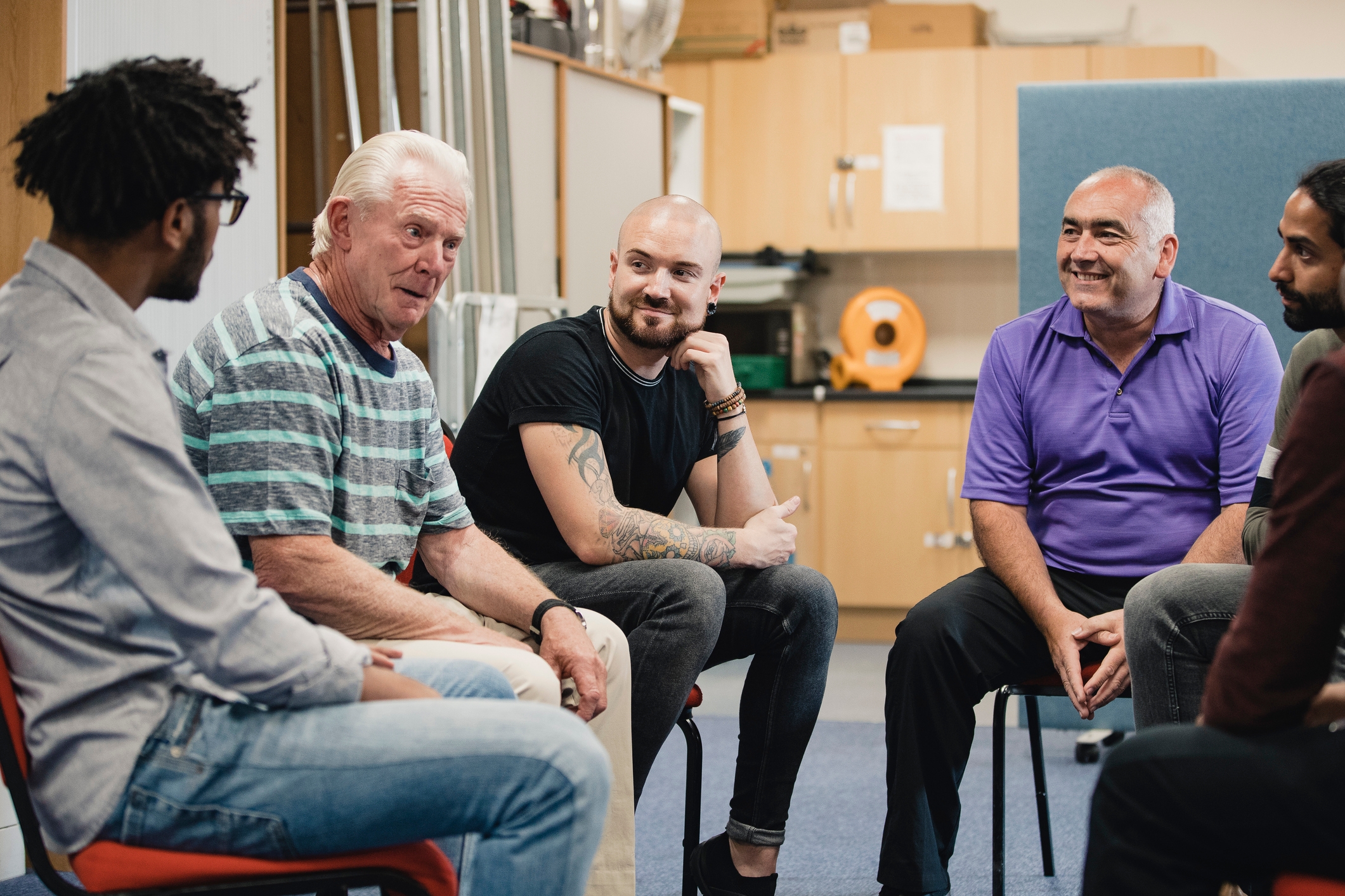 A group of five people sitting in a circle, engaged in a casual and friendly discussion in an indoor setting