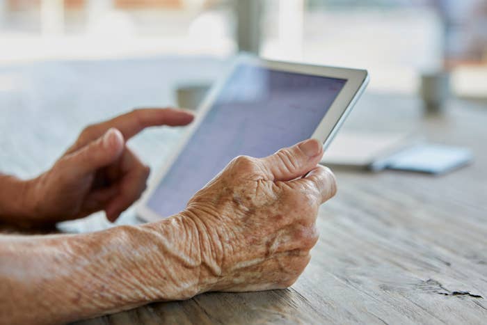 Older adult's hands using a tablet at a wooden table, emphasizing the ease of technology use across different ages