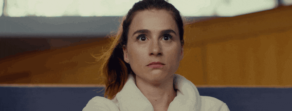 Person sitting with a surprised expression wearing a robe while getting their nails done, hands outstretched in a salon setting