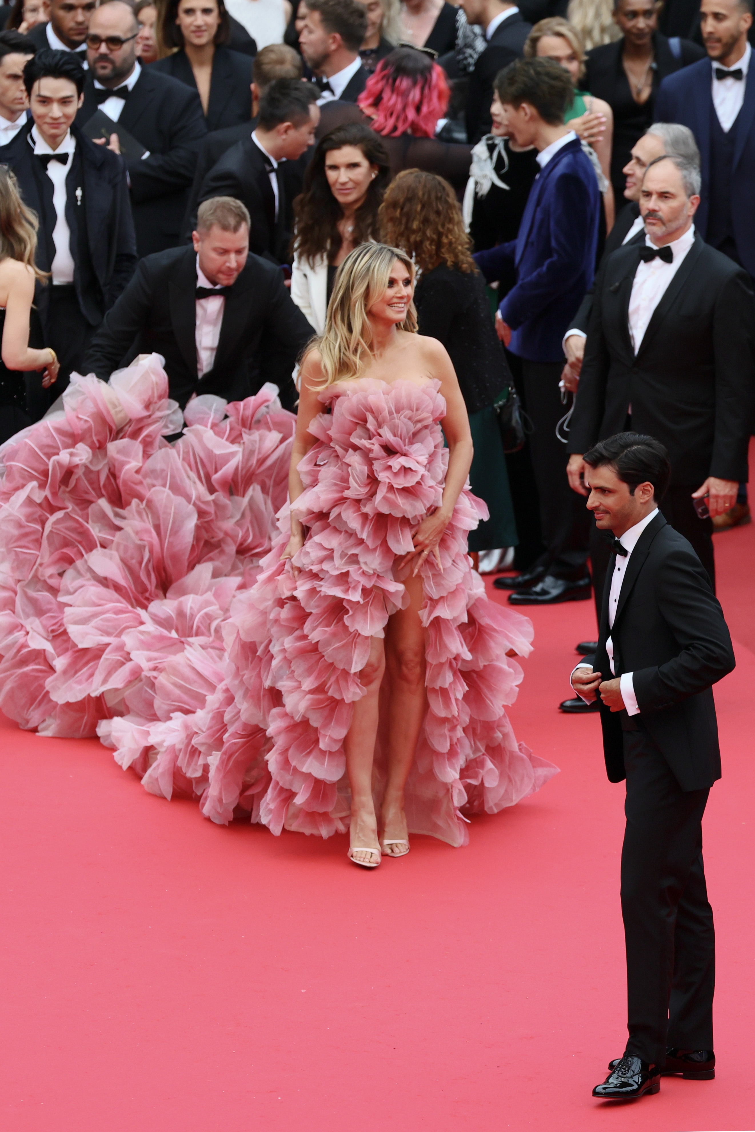 Heidi Klum in a voluminous ruffled gown on a red carpet, surrounded by others in formal attire