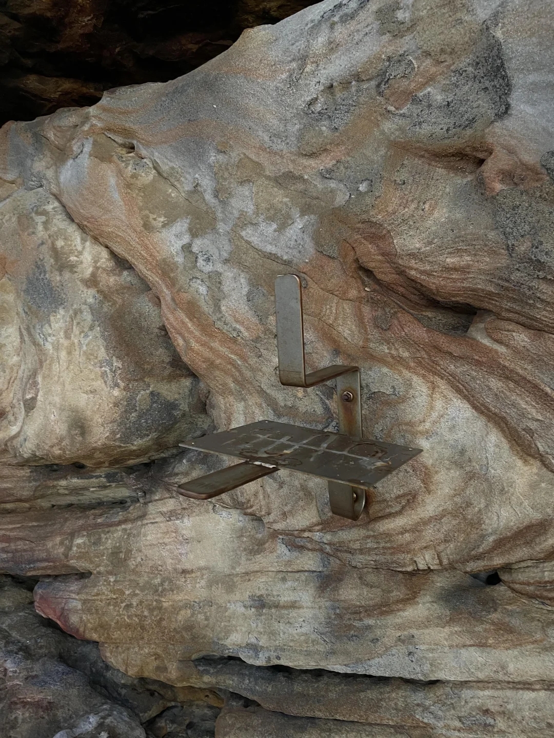 Metal sculpture embedded in a rock, resembling a small chair or abstract shape, blending with the natural stone texture