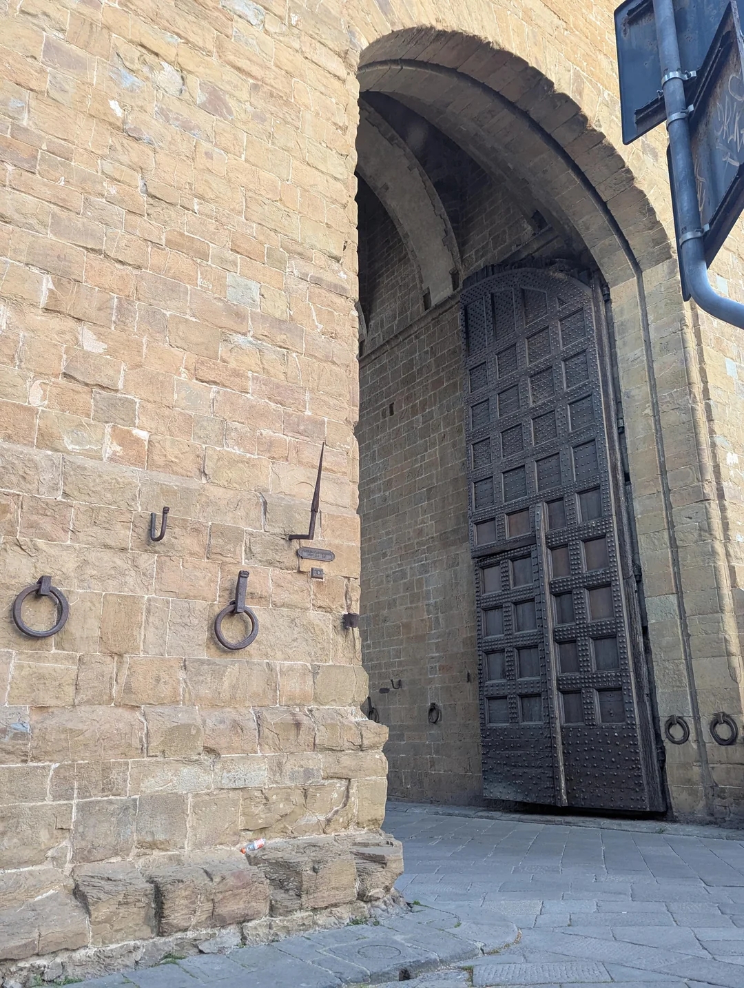 Ancient stone archway with large wooden doors ajar, surrounded by medieval iron fittings on the wall
