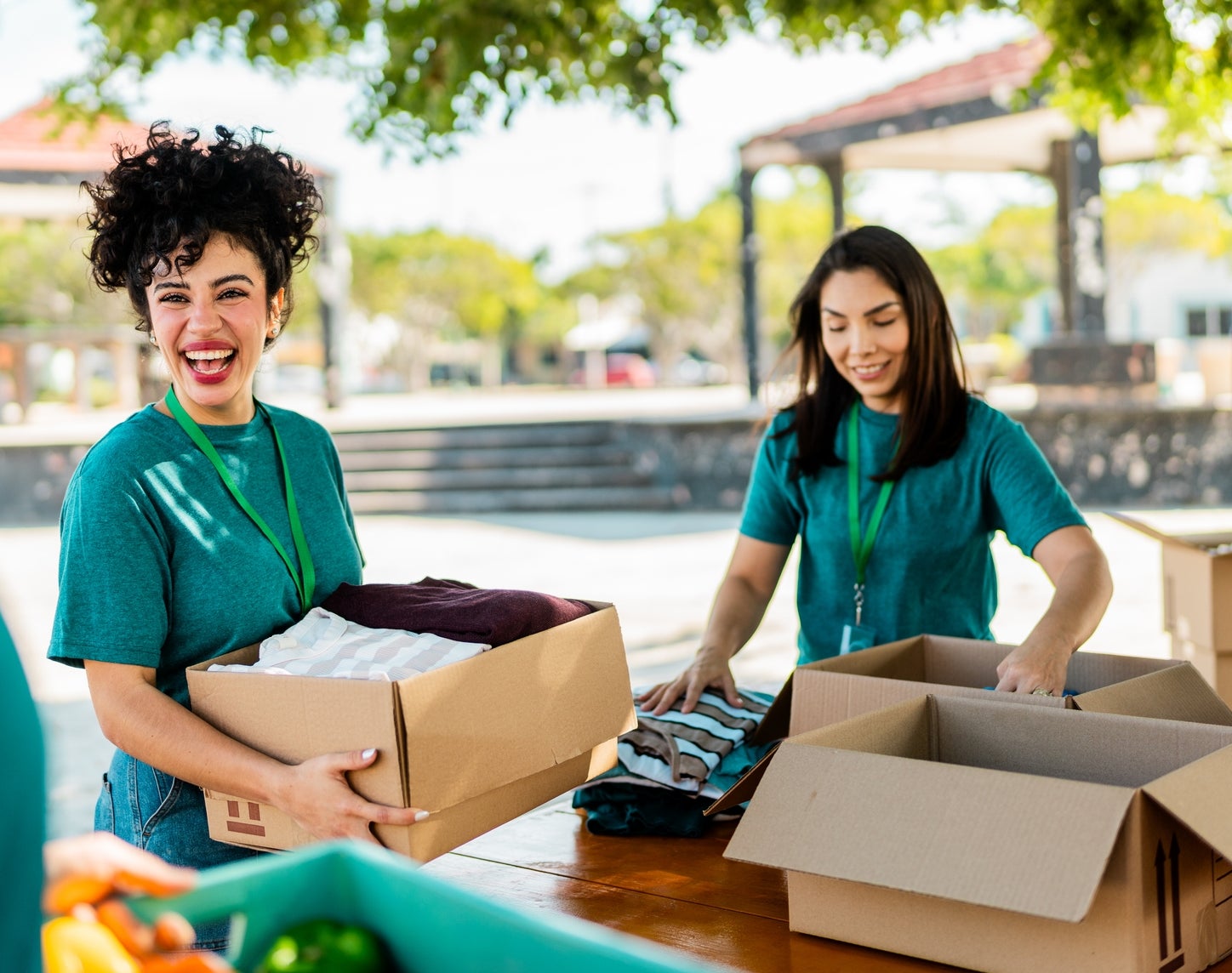 People in matching shirts happily volunteer outdoors, sorting and packing boxes with clothes and supplies