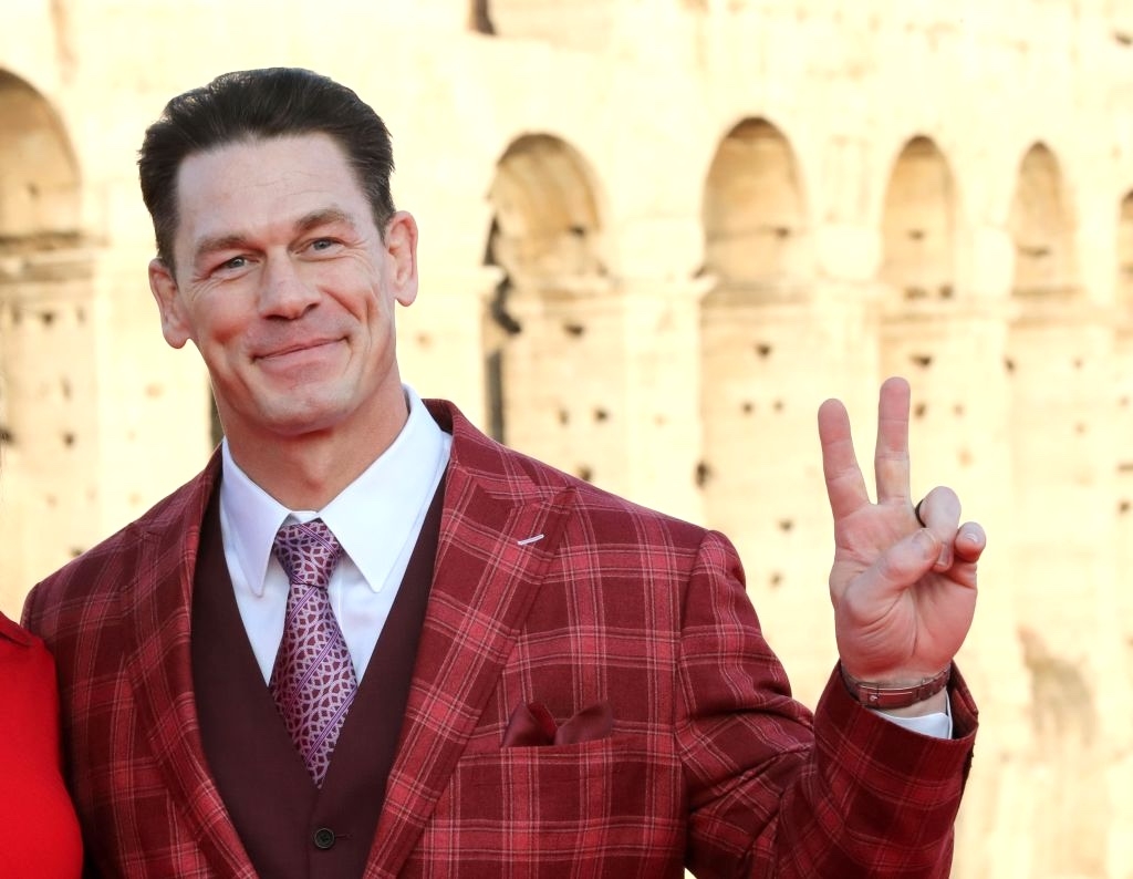 Person in a checkered suit poses with a peace sign in front of an ancient architecture backdrop