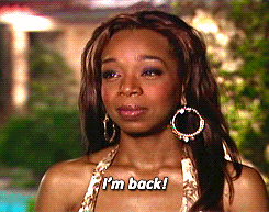 Person wearing hoop earrings and patterned top smiles slightly, text reads "I'm back!"